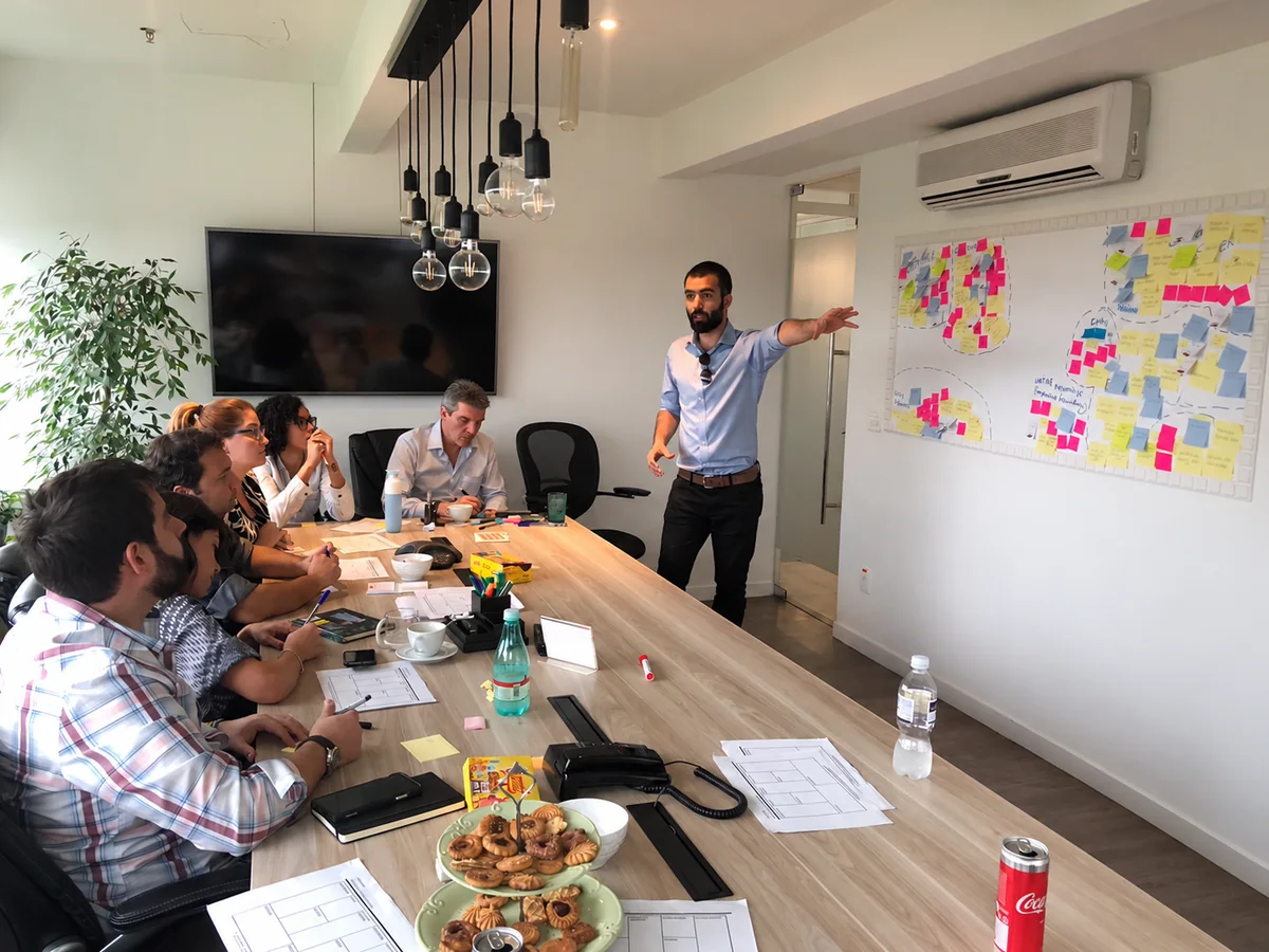 Saad leading a team workshop beside a whiteboard; photograph edited to remove the rightmost presenter